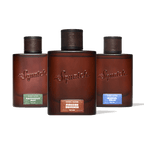 Three Squatch fragrance bottles arranged in a row against a solid green background. The center bottle is upright and labeled 'Squatch Fireside Bourbon', while the left and right bottles are slightly angled backward and labeled 'Squatch Rainforest Mist' and 'Squatch Glacial Falls' respectively.