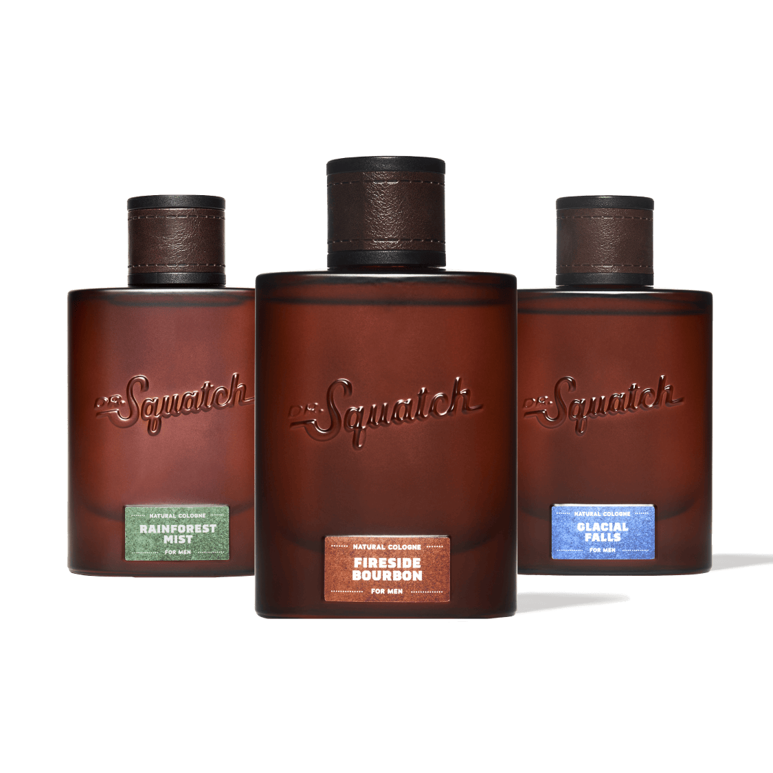 Three Squatch fragrance bottles arranged in a row against a solid green background. The center bottle is upright and labeled 'Squatch Fireside Bourbon', while the left and right bottles are slightly angled backward and labeled 'Squatch Rainforest Mist' and 'Squatch Glacial Falls' respectively.